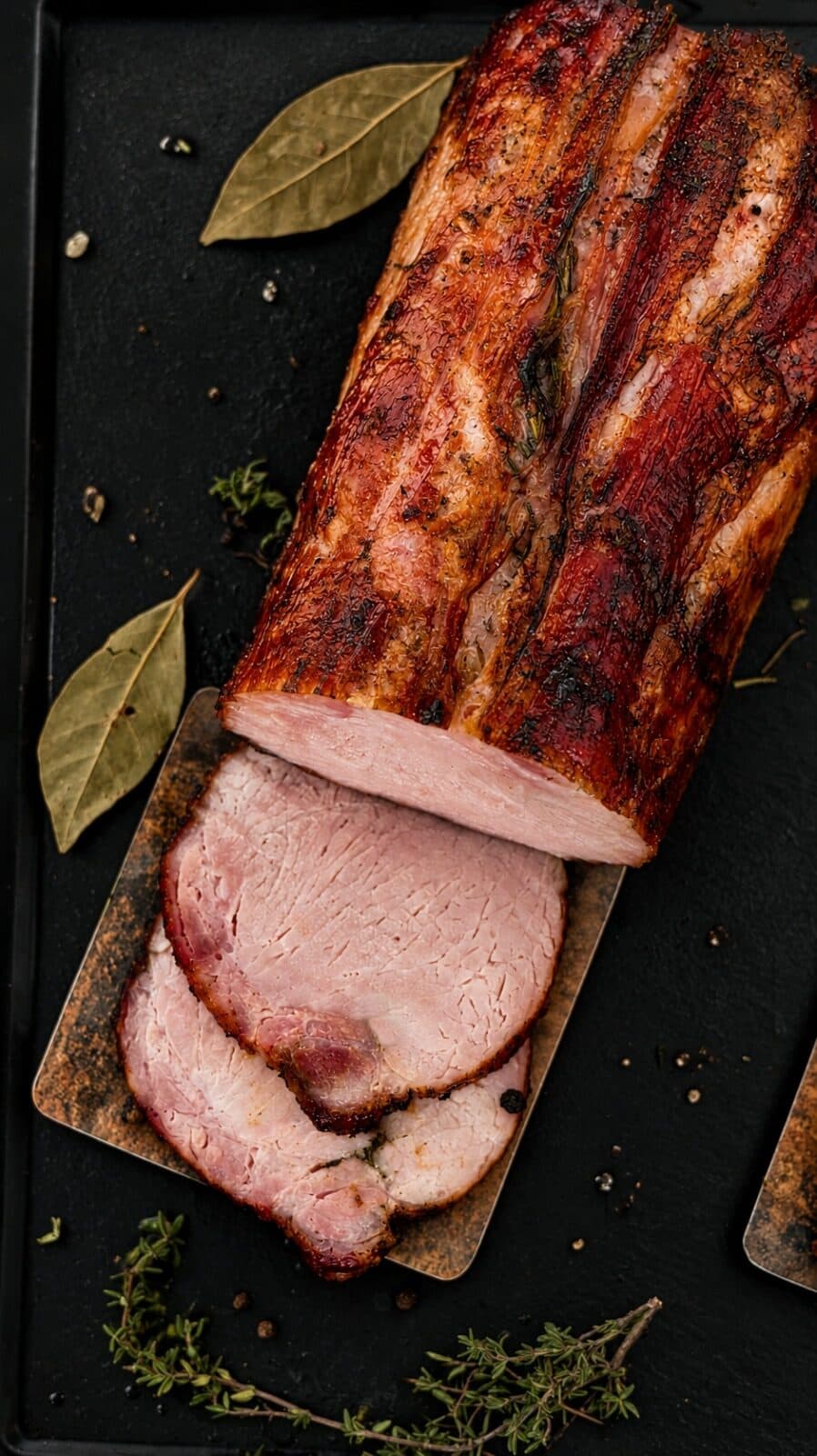 Lomo de cerdo ahumado de corteza rojiza con dos rodajas rosadas sobre tabla