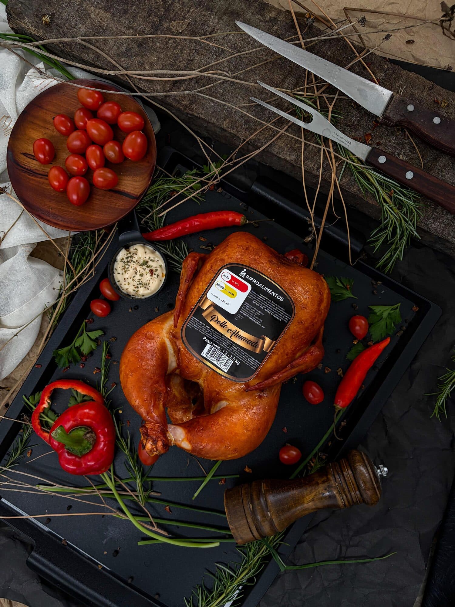Pollo ahumado etiquetado visto en ángulo junto a tomates cherry, pimiento y pimentero
